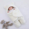 Bébé paisible allongé sur un lit, enveloppé dans un nid d'ange blanc, à côté d'une peluche ourson, illustrant le confort et la douceur que ces accessoires pour bébé apportent.