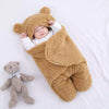 Bébé paisible allongé sur un lit, enveloppé dans un nid d'ange marron, à côté d'une peluche ourson, illustrant le confort et la douceur que ces accessoires pour bébé apportent.