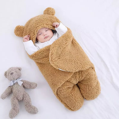 Bébé paisible allongé sur un lit, enveloppé dans un nid d'ange marron, à côté d'une peluche ourson, illustrant le confort et la douceur que ces accessoires pour bébé apportent.
