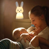 Veilleuse en forme de lapin sur un chevet éclairant une maman allaitant son bébé.