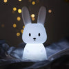 Veilleuse en forme de lapin illuminée en blanc dans une ambiance féerique.