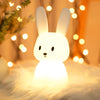 Veilleuse en forme de lapin illuminée d'une couleur chaude dans une ambiance féerique.